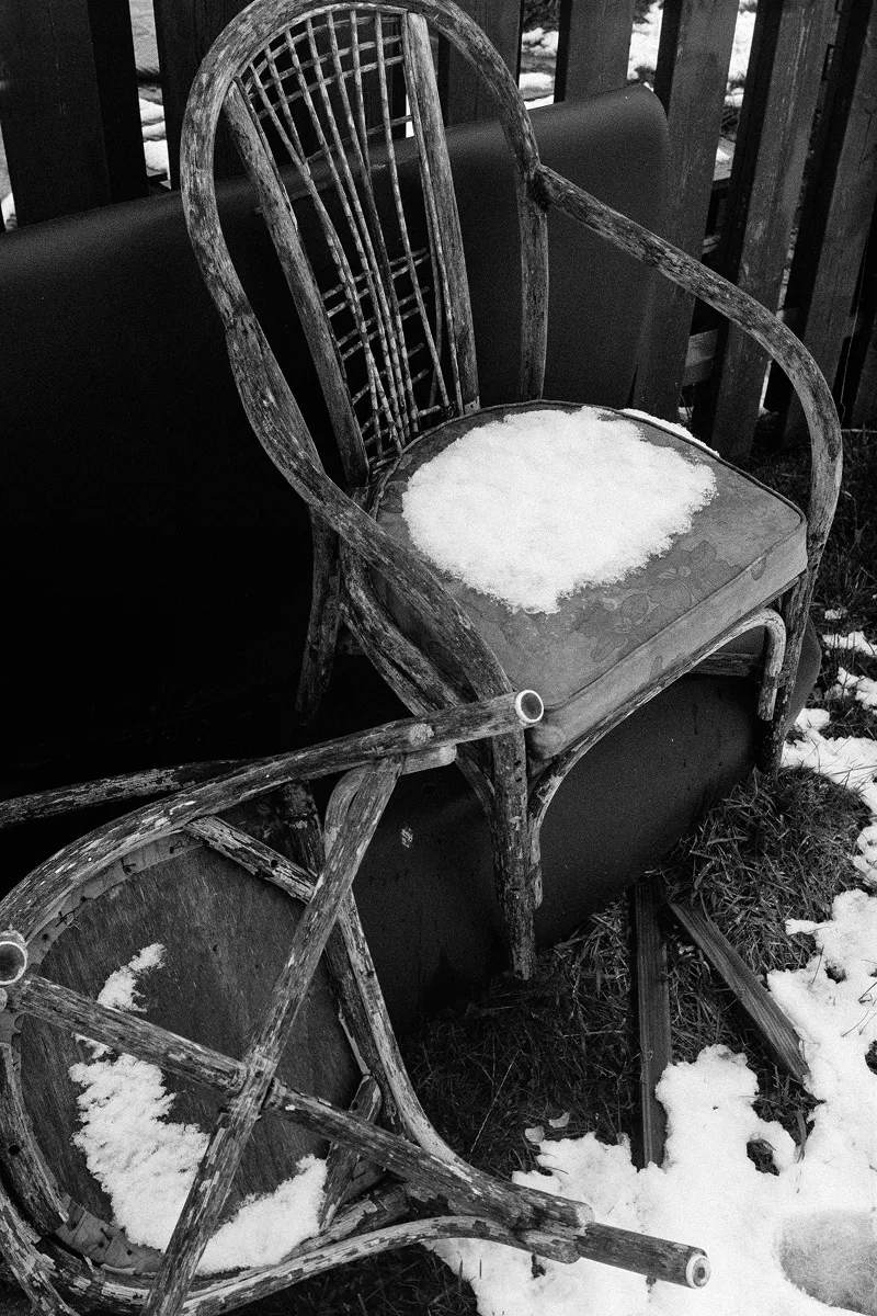 Weathered vintage chairs stacked outdoors with snow on seats