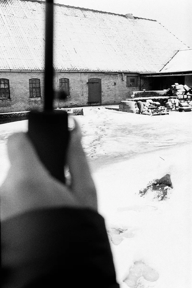 View from under umbrella of snowy farmyard courtyard with brick barn and stacked firewood
