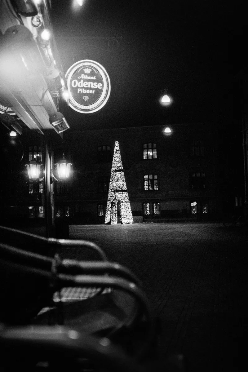 Illuminated Christmas tree in town square at night with Odense Pilsner sign in foreground