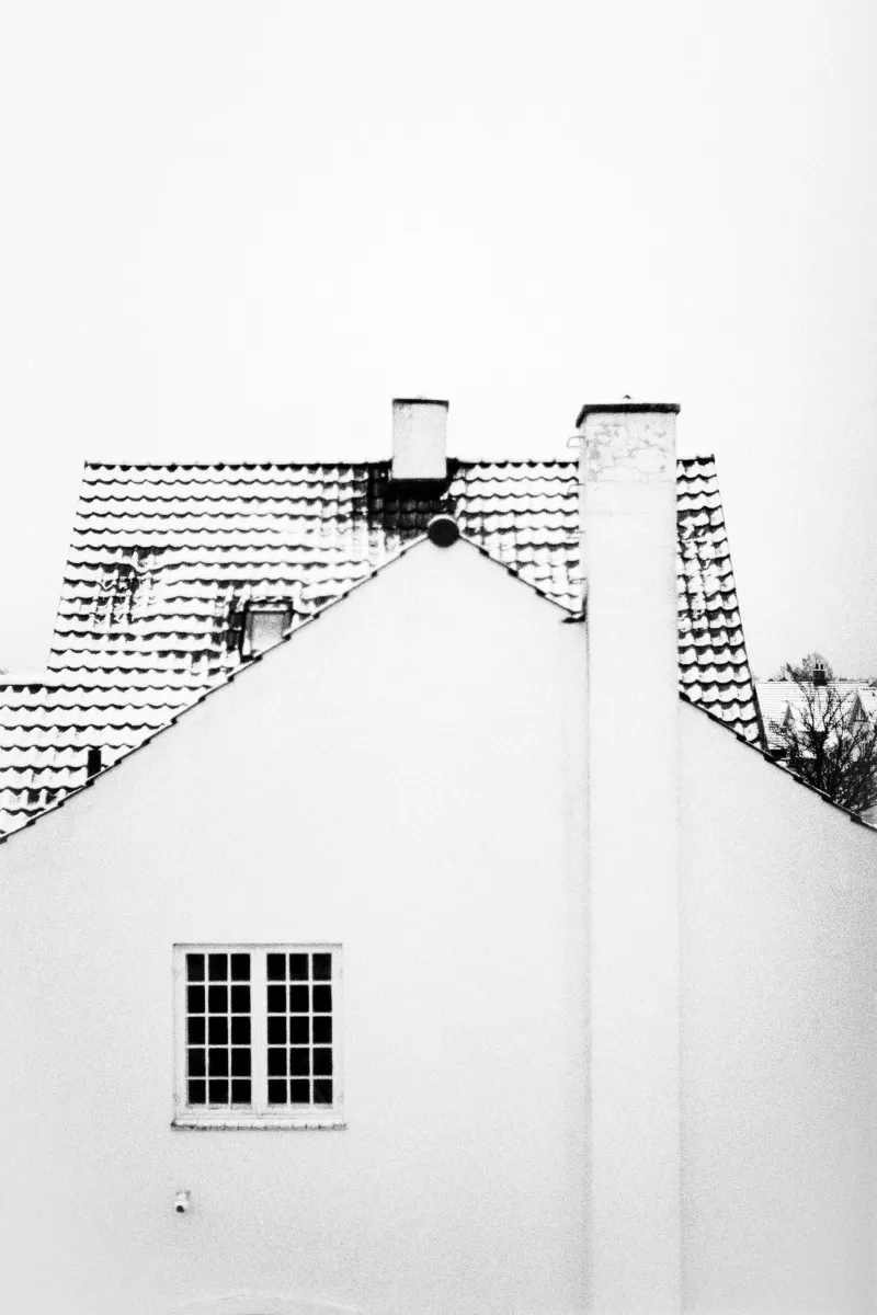 Minimalist white house facade with tiled roof and two chimneys against overcast sky