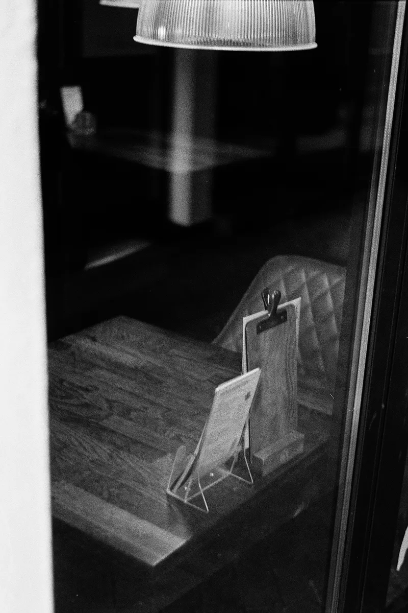 Restaurant menu card on small stand viewed through window with pendant light above