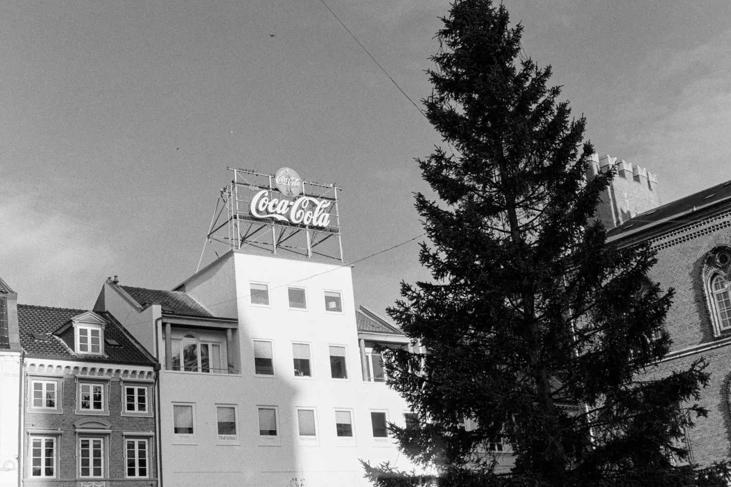Vintage Coca-Cola rooftop sign on white building with Christmas tree in foreground