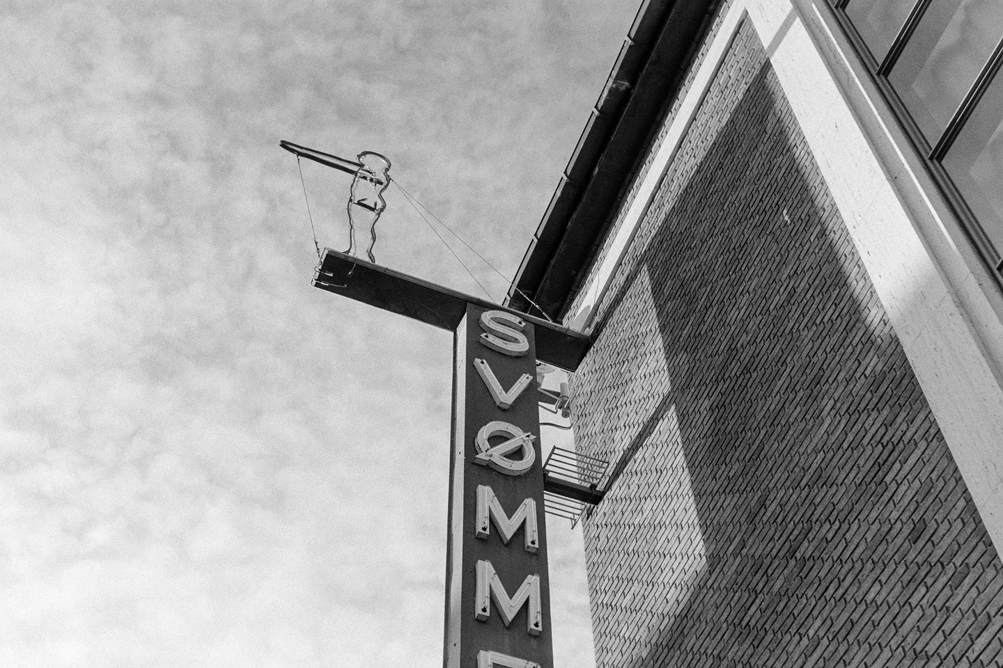 Vertical SVØMME swimming pool sign with swimmer icon on textured building facade