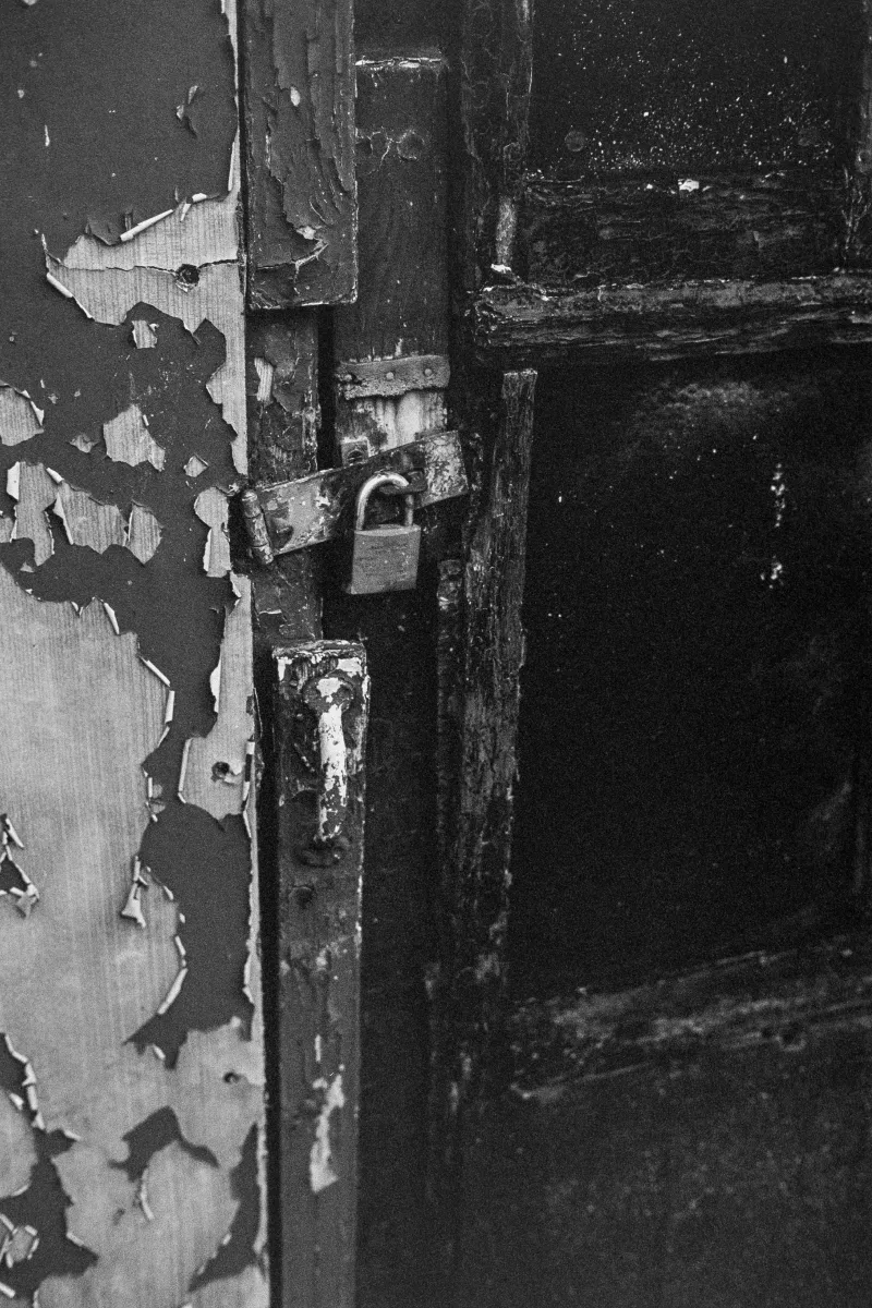 Detail of an old wooden door with handle and padlock. The paint is already peeling off the wood.