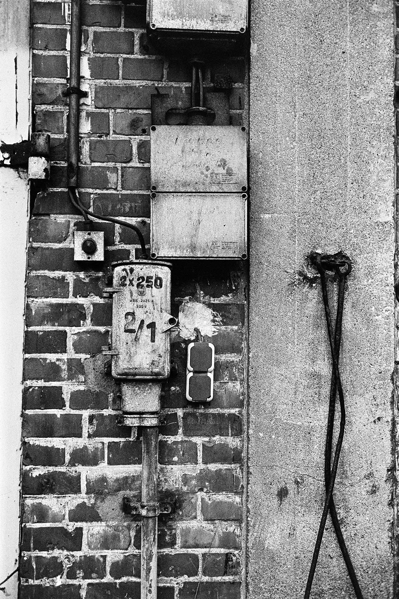 Front view of old electrical boxes, cables, and switches on a brick and plaster wall.