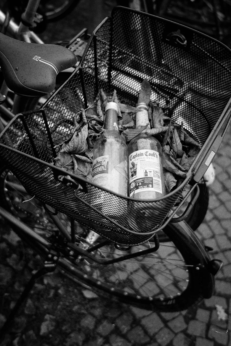 Overhead view of bicycle basket containing Captain Cook's and Pfeffi bottles with autumn leaves