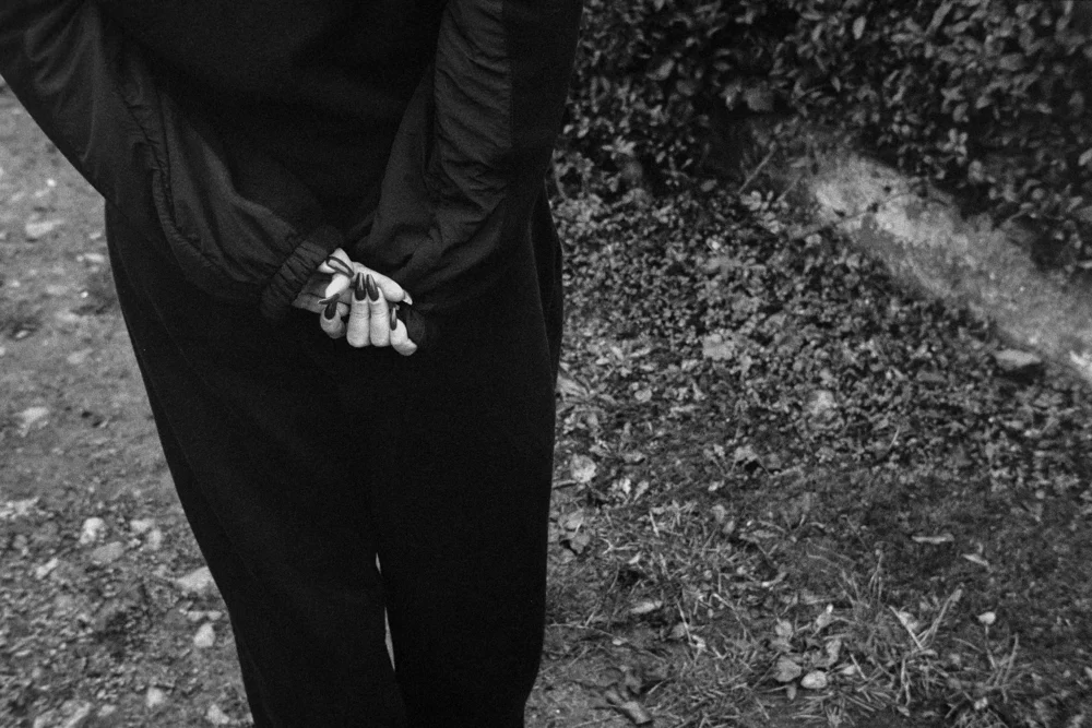 Person with manicured nails and crossed fingers behind back standing on garden path