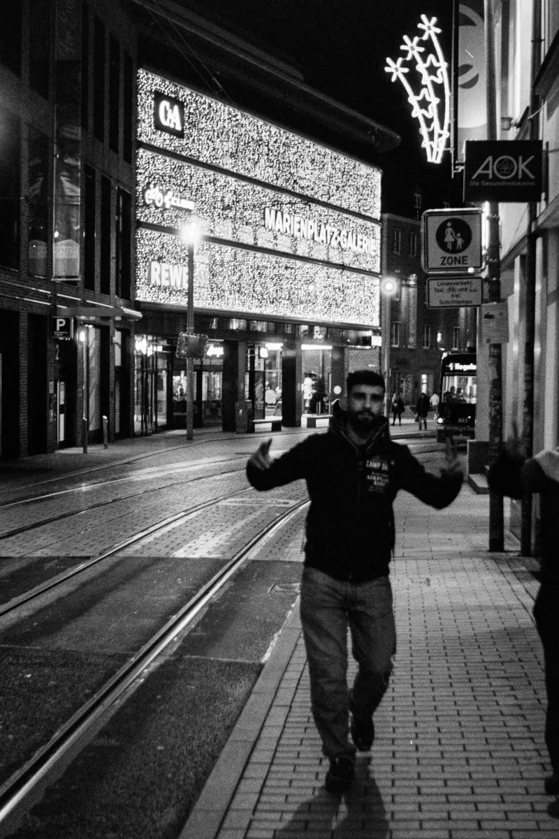 Person gesturing on night street in front of illuminated Marienplatz Galerie shopping mall