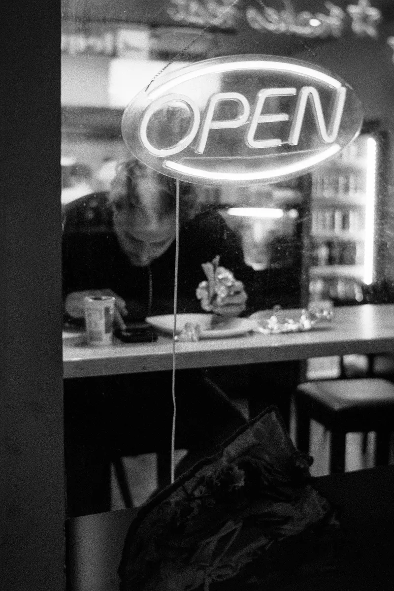 Neon OPEN sign in Döner Kebab shop window with customer eating and looking at smartphone