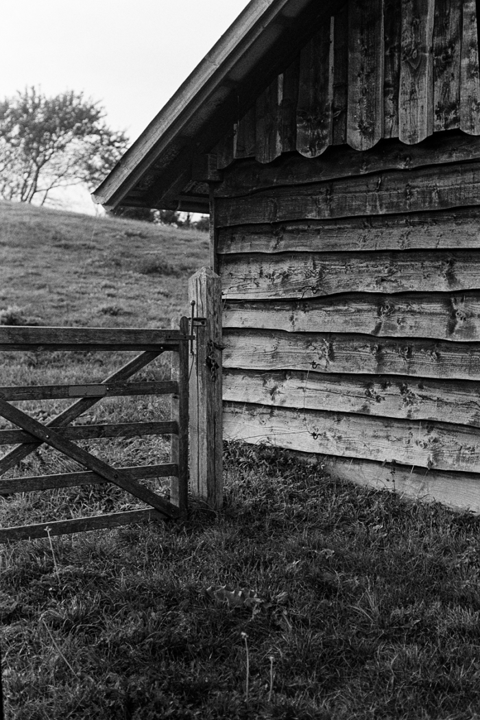 Weathered wooden barn with corrugated roof and wooden gate on hillside