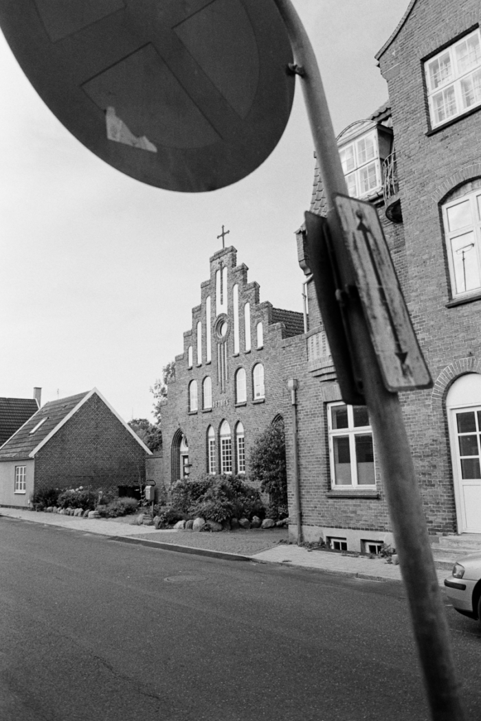 Brick church with stepped gable facade and cross, stop sign in foreground on residential street