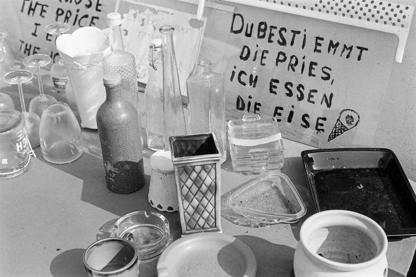 Messy table with empty bottles and glasses and a humorous handwritten sign promoting the “pay what you want” principle.