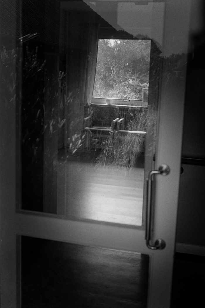 View through entrance of abandoned nursing home with old armchairs and overgrown garden