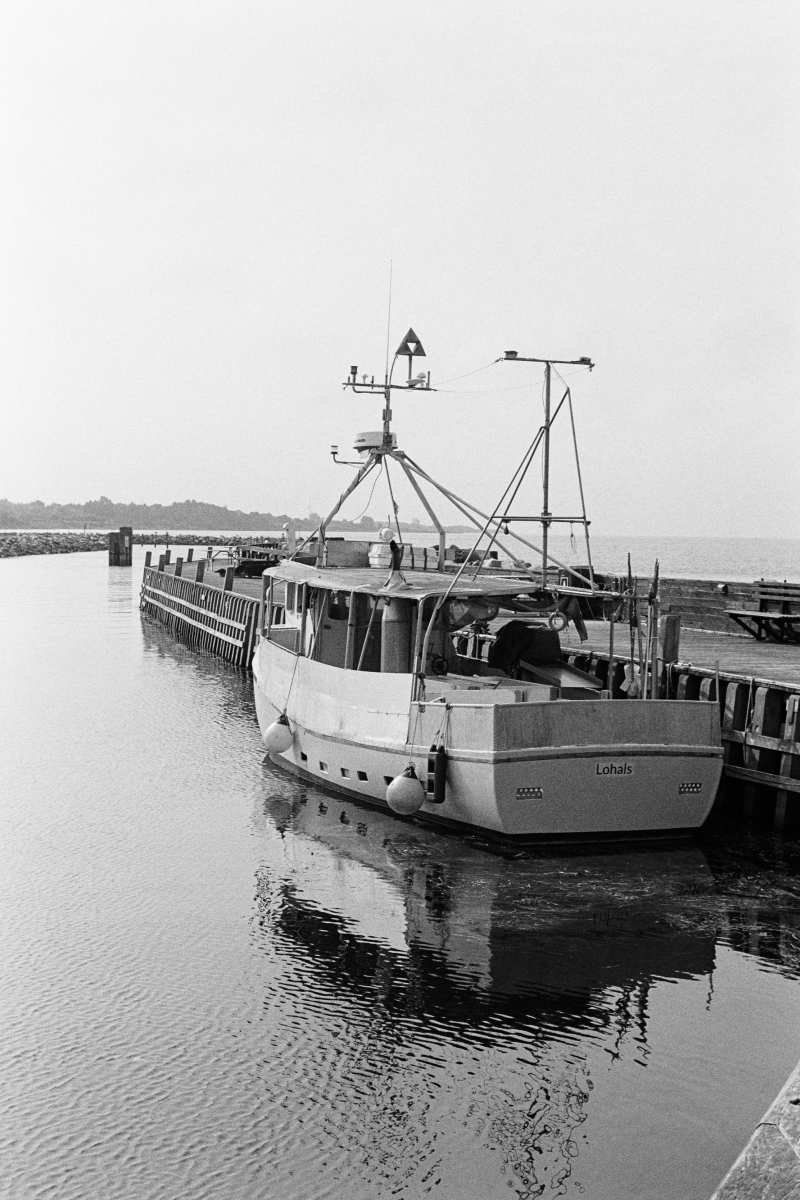 Fishing boat named Lohals moored at wooden pier with mast and equipment