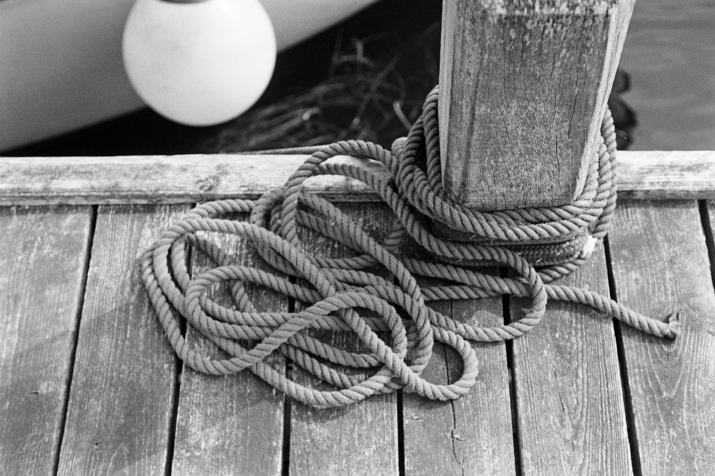 Thick rope coiled around wooden mooring post on weathered dock