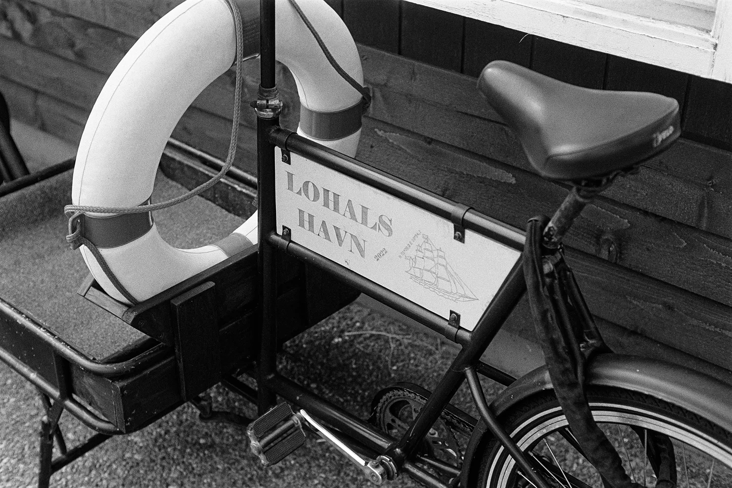 B&W detail of a harbor cargo bike with a white life ring and a "Lohals Havn" sign featuring a vintage ship illustration.