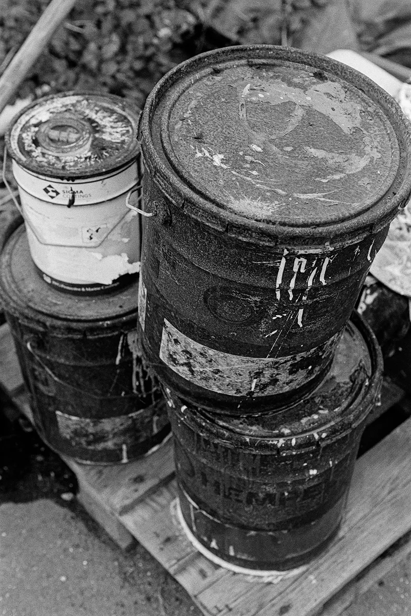 High-angle B&W shot of stacked, rusty paint buckets on a wooden pallet, showing weathered textures and industrial wear.