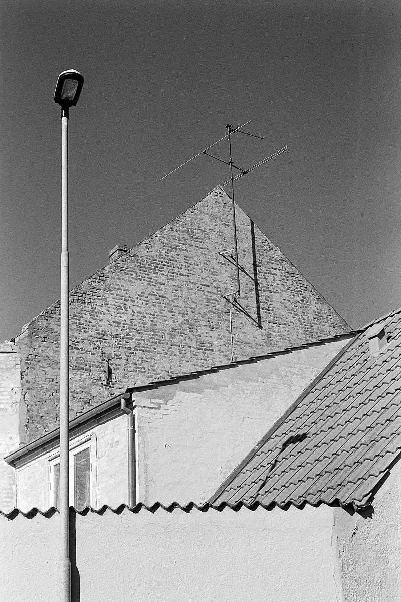 Minimalist B&W architectural view of a brick house gable with a tall TV antenna and a sleek street lamp against a dark sky.