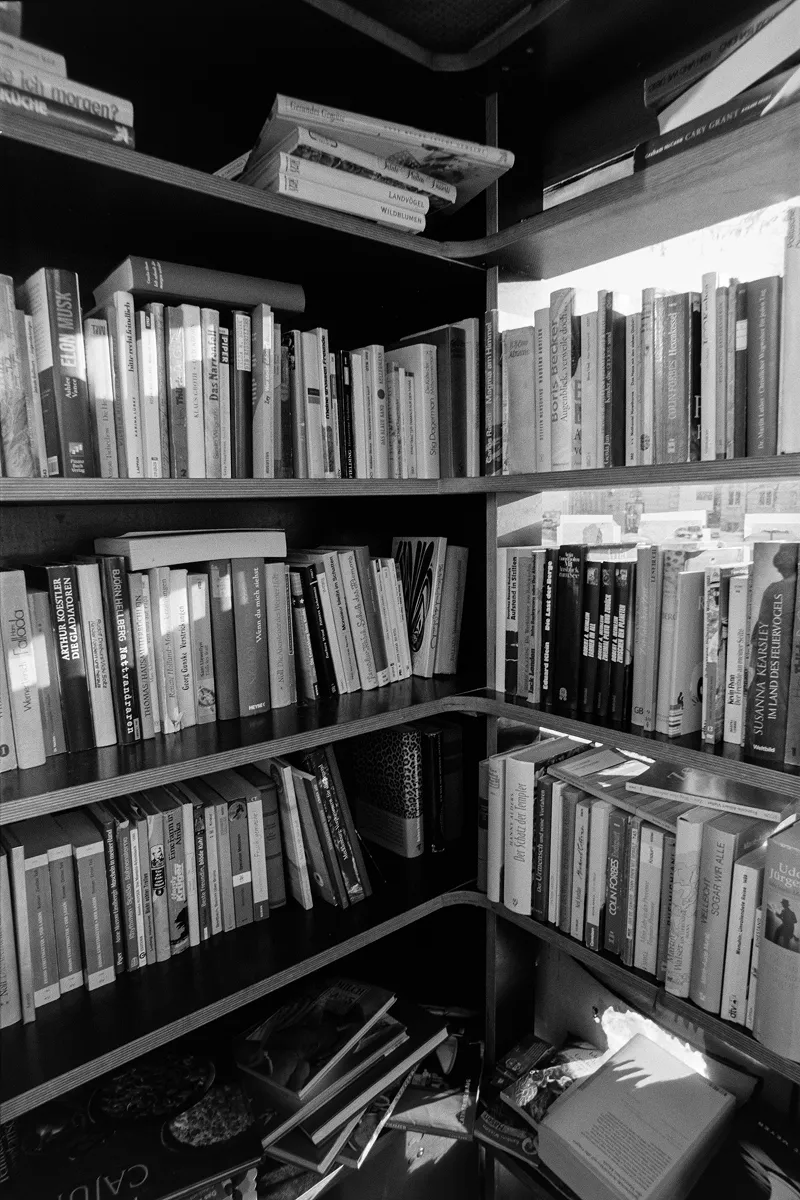 Wide-angle B&W shot of a repurposed telephone booth used as a public bookcase, filled with titles and harsh shadows.