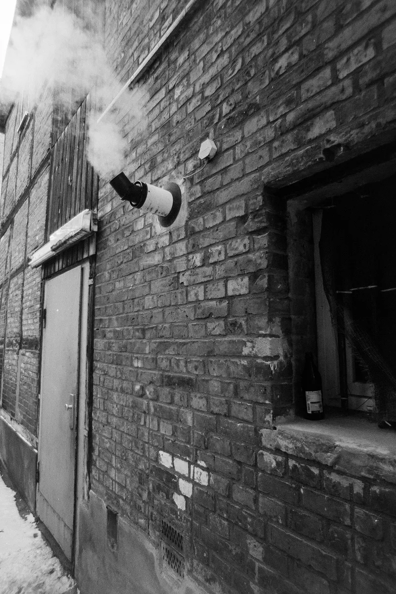 Minimalist B&W shot of steam rising from an exhaust pipe on an old brick wall, highlighting weathered urban textures.