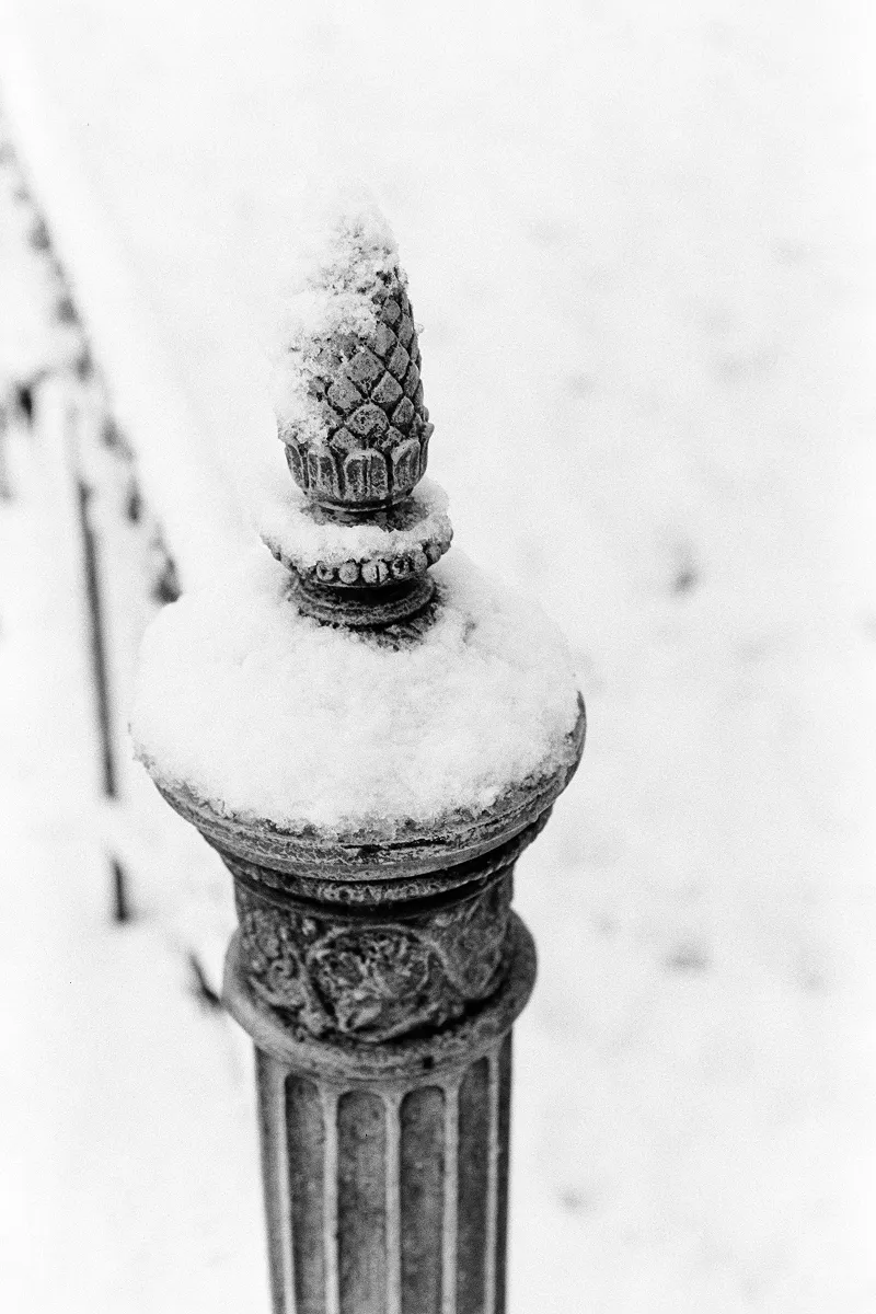 Close-up of a decorative metal fence finial topped with a neat cap of fresh white snow.