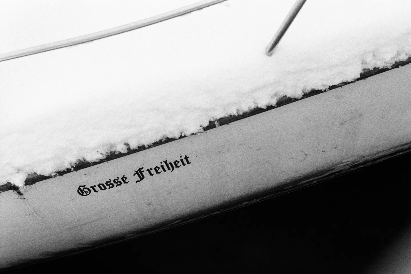 Minimalist B&W shot of a boat hull with "Grosse Freiheit" in gothic script, topped with a crisp layer of snow.