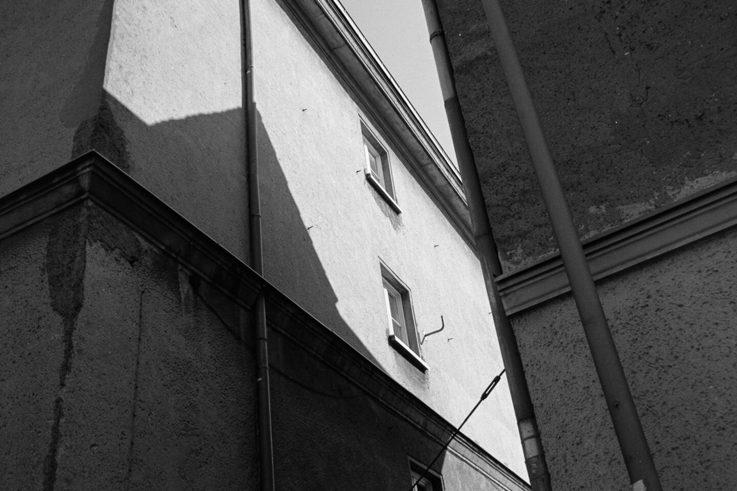 B&W film photo of sharp architectural angles, showing textured building walls and windows. High contrast, grainy look.