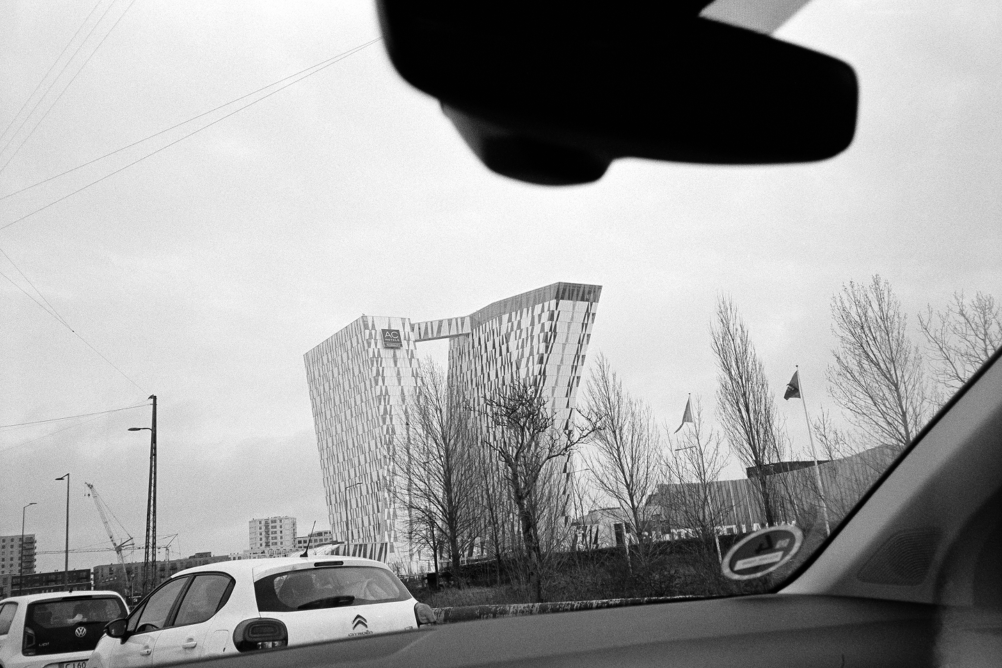 B&W view from a car of the leaning Bella Sky Hotel towers in Copenhagen. Grainy film aesthetic under a cloudy Danish sky.