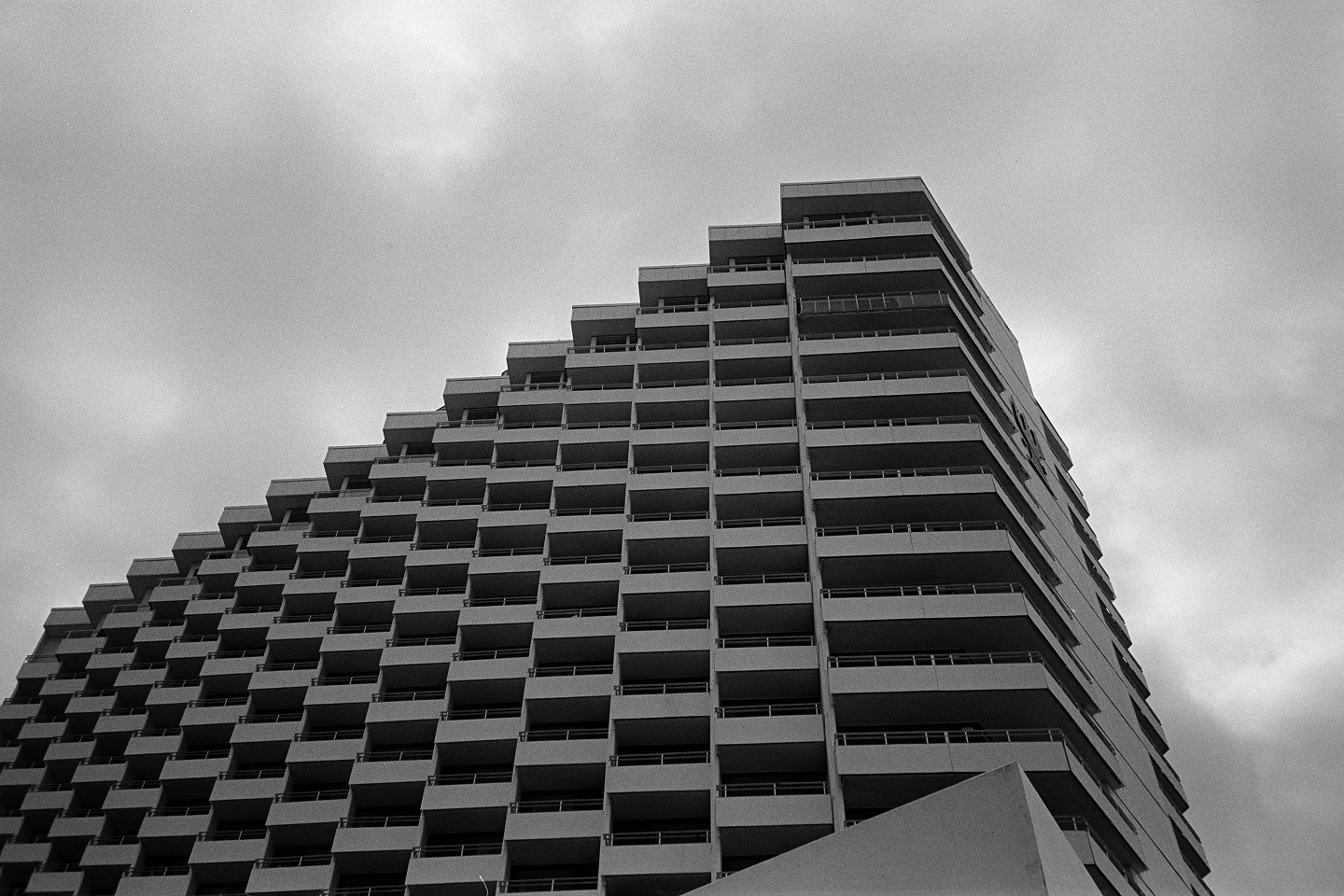 B&W film photo featuring the sharp geometric balconies of a tall hotel building against a flat, overcast sky.